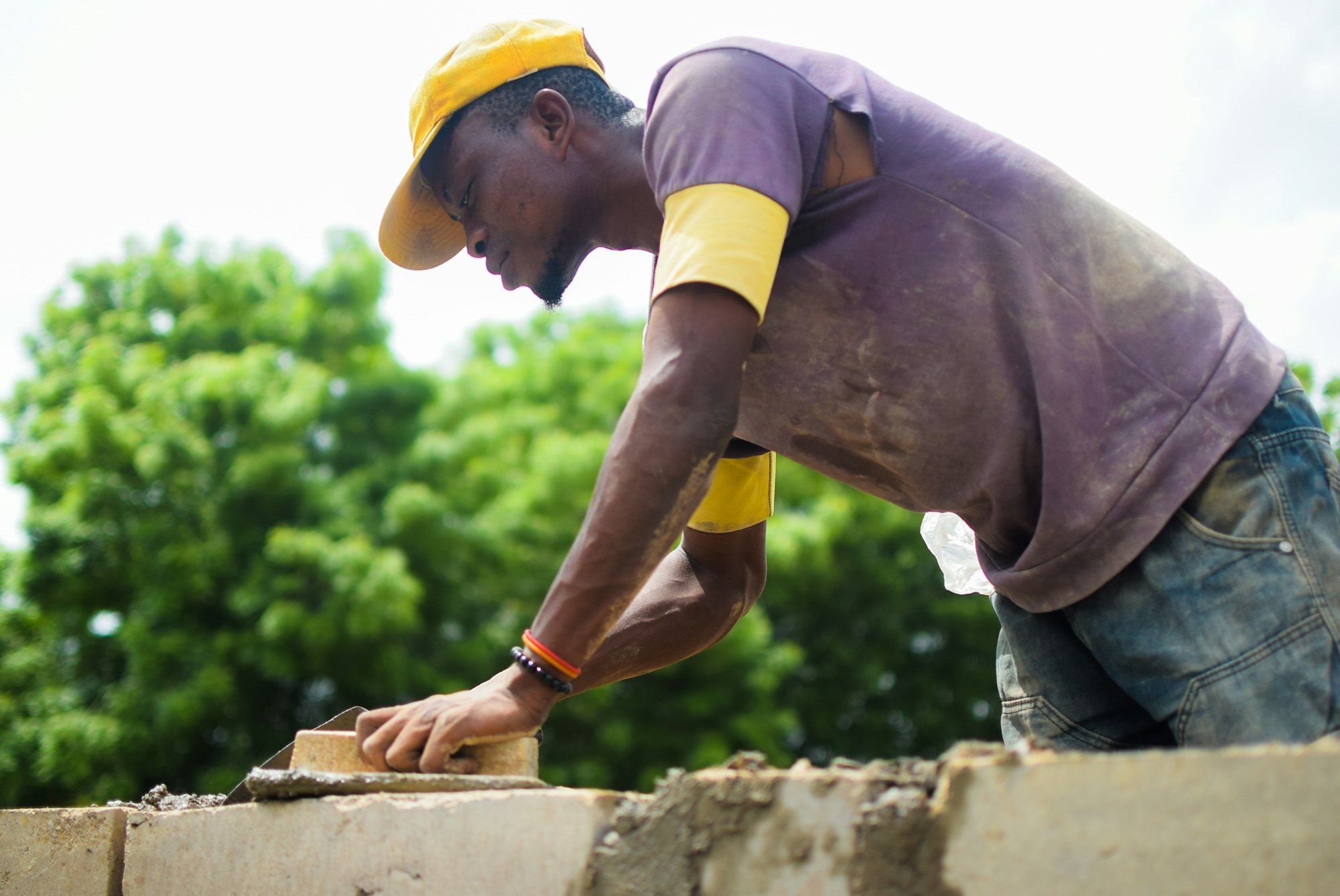 Mason in a yellow cap laying bricks on a wall outdoors