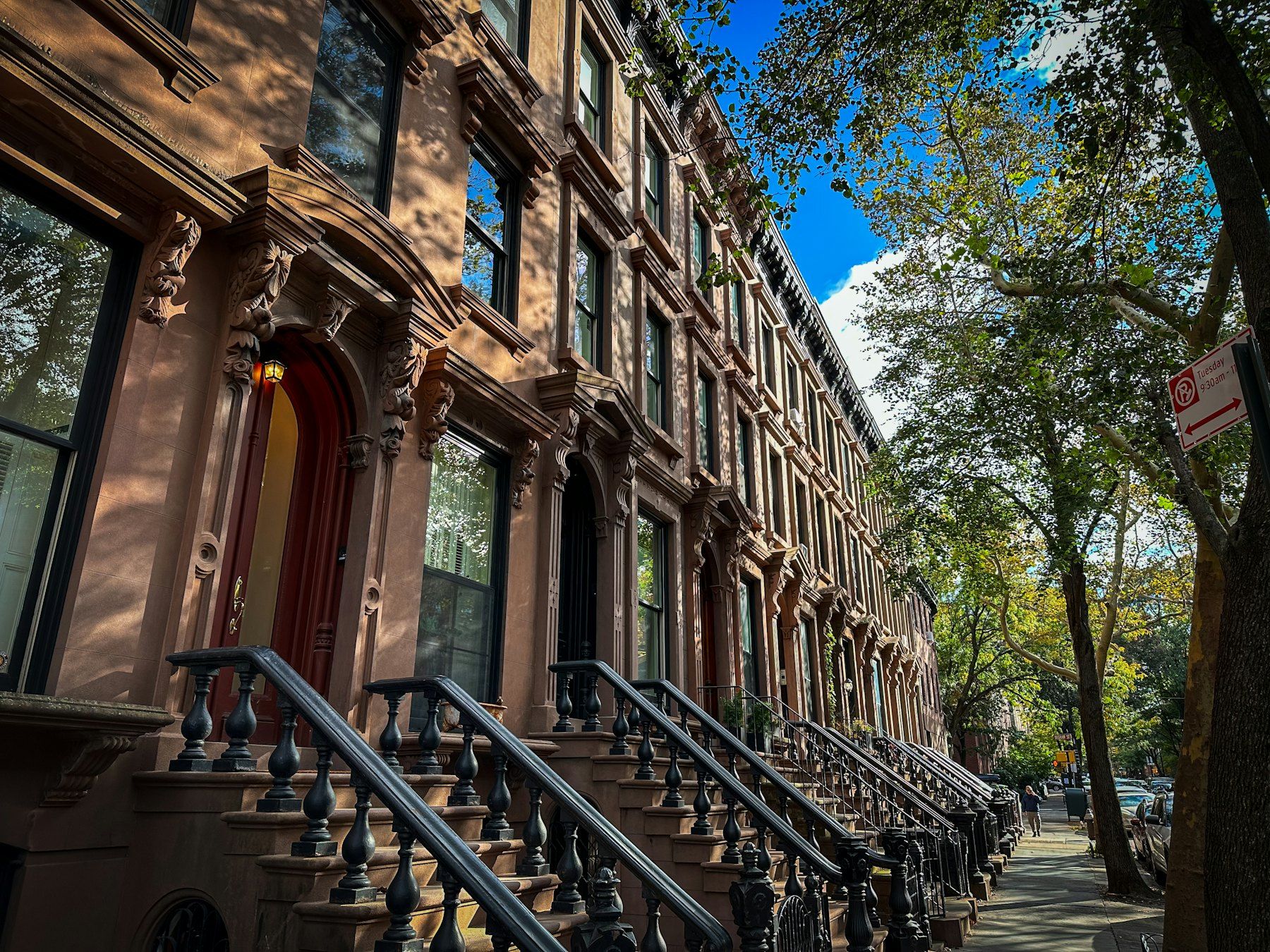 Row of brownstone townhouses with iron-railed stoops on a tree-lined street