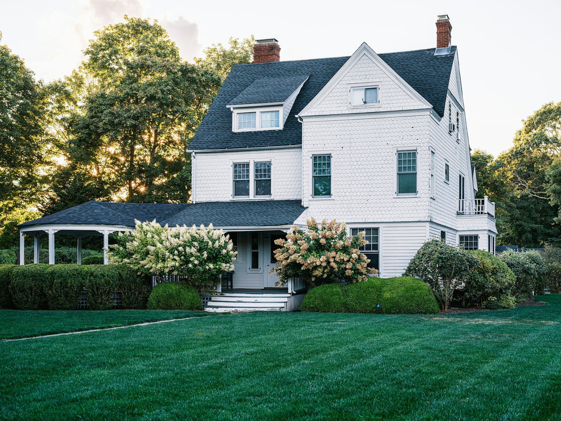 White three-story house with a dark roof, a brick chimney and a green lawn